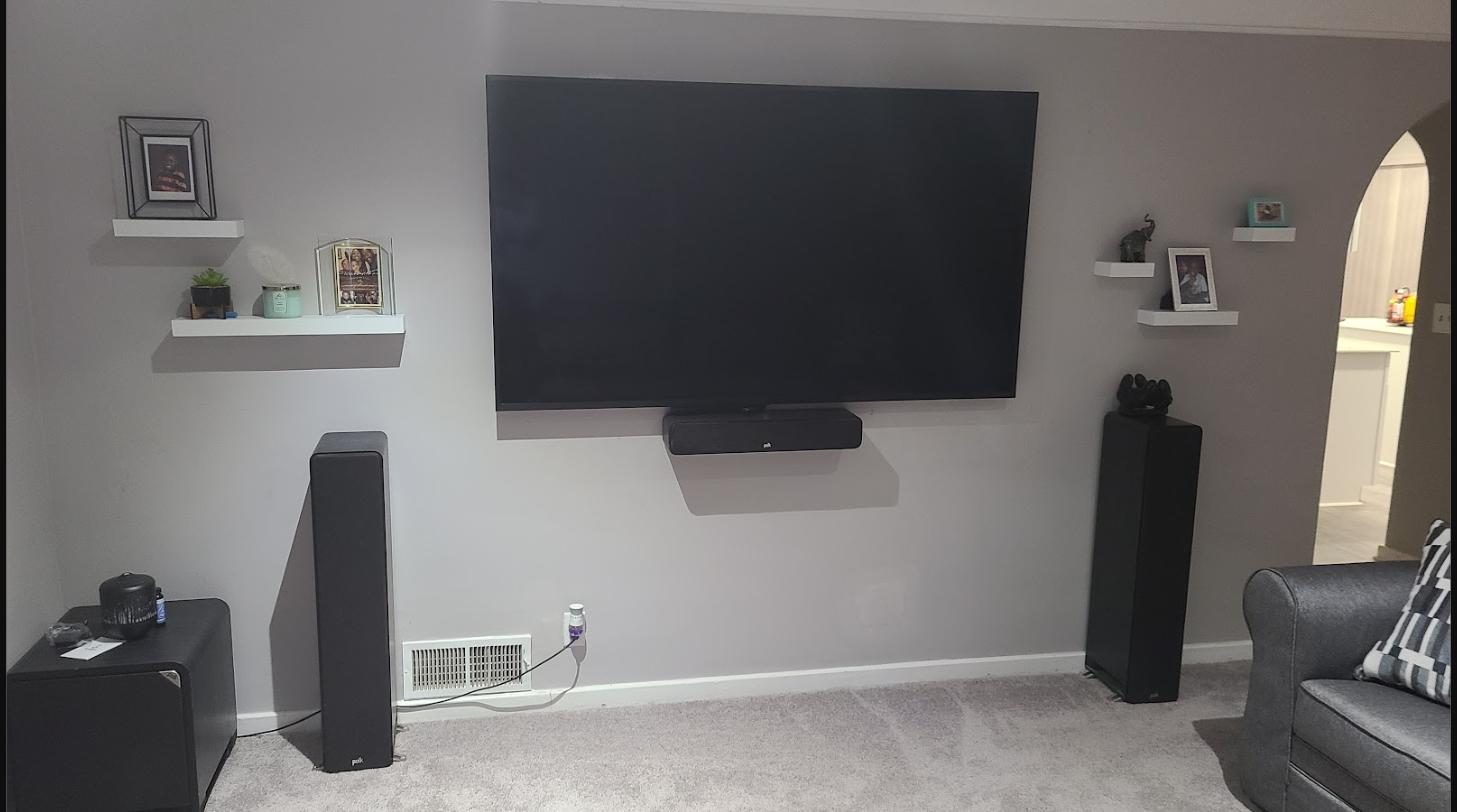 Floor-standing surround sound speakers installed beside a wall-mounted TV and soundbar